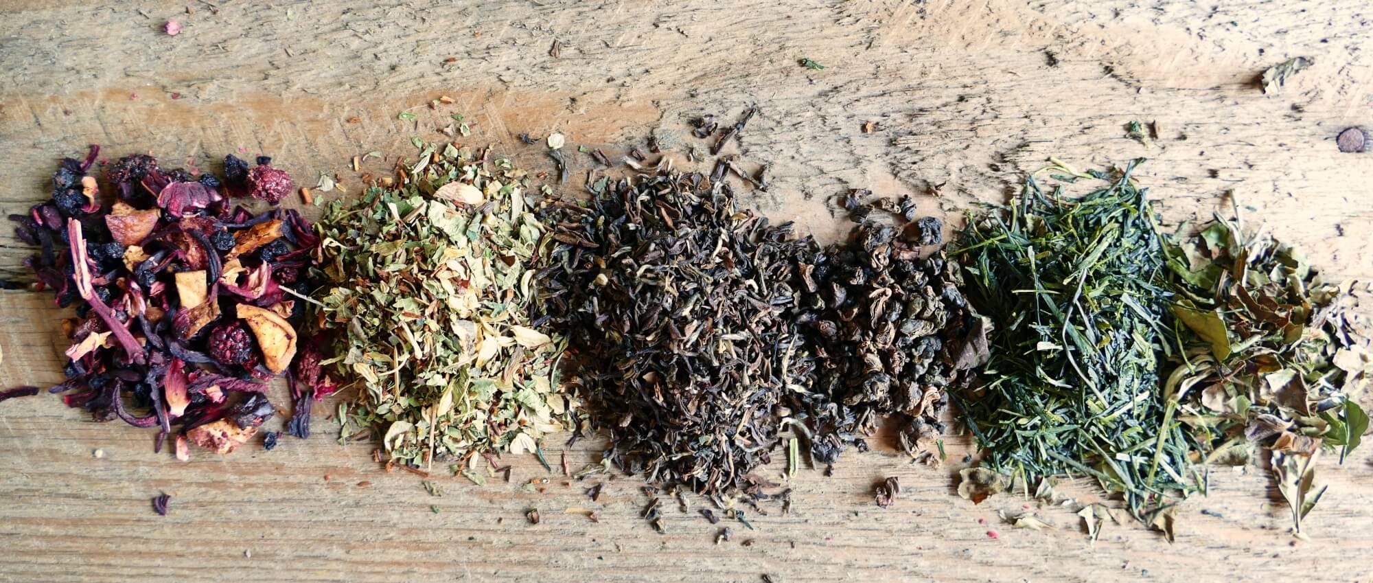 Verschiedene Teesorten liegen auf einem Brett: Fürchtete, Kräutertee, schwarzer Tee, grüner Tee